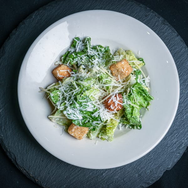 A white plate filled with Caesar salad, topped with croutons and shredded Parmesan cheese.