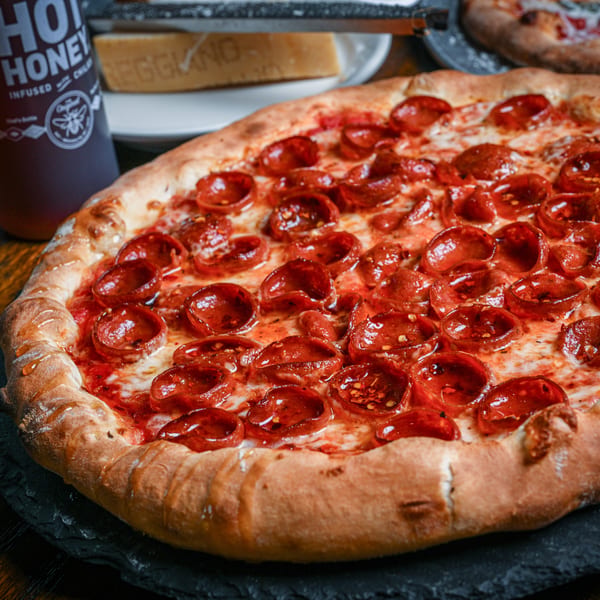A pepperoni pizza with hot honey drizzled on top, served on a dark slate board.