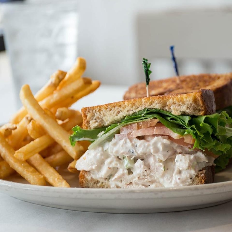 Chicken salad sandwich on toasted bread with lettuce, tomato, and a side of french fries.
